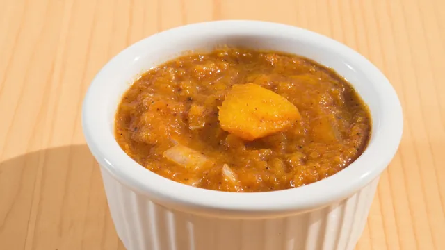 A white ramekin of thick pumpkin curry soup on a wooden table