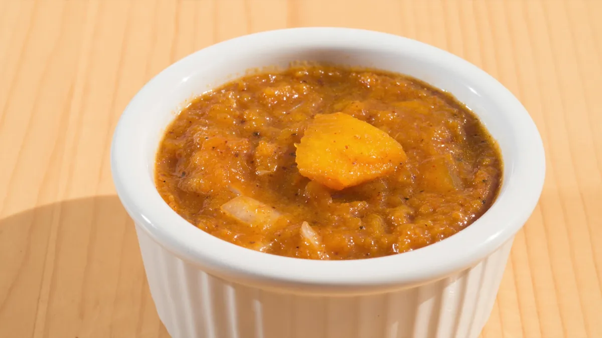 A white ramekin of thick pumpkin curry soup on a wooden table