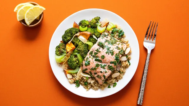Salmon fillet with broccoli and grains on a white plate against an orange background