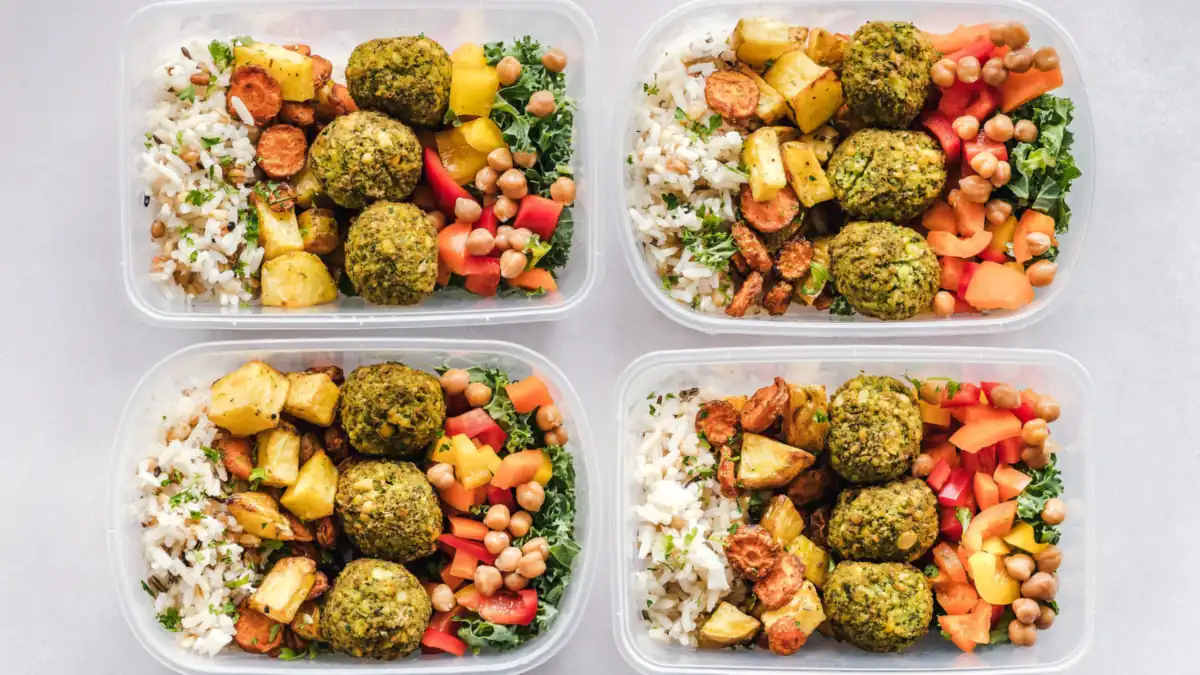 Four meal prep containers filled with rice, roasted vegetables, chickpeas and herb falafel