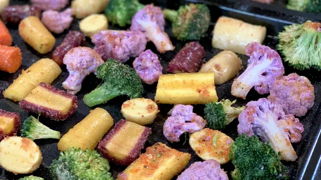 Broccoli, carrots, potatoes and purple cauliflower roasting on a sheet pan