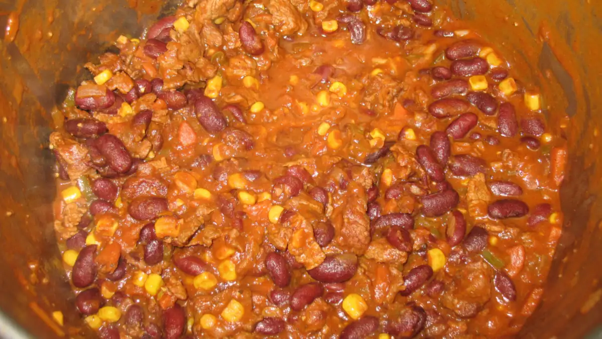 A pot of chili with kidney beans and corn simmering on the stove